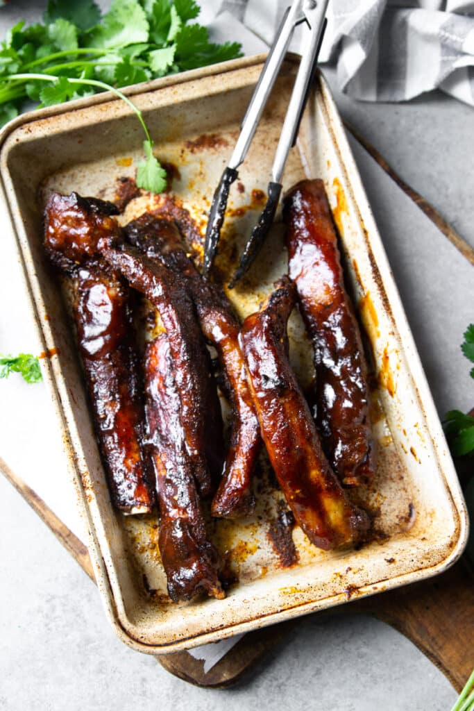 spare ribs coated in bbq sauce in a metal baking dish.