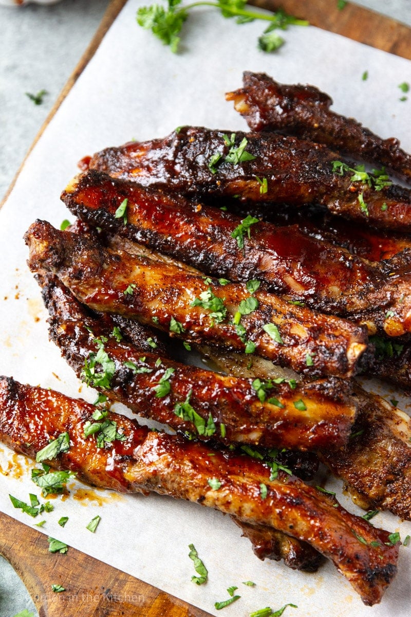 close up on barbecue spare ribs piled on top of each other on a sheet of parchment paper.