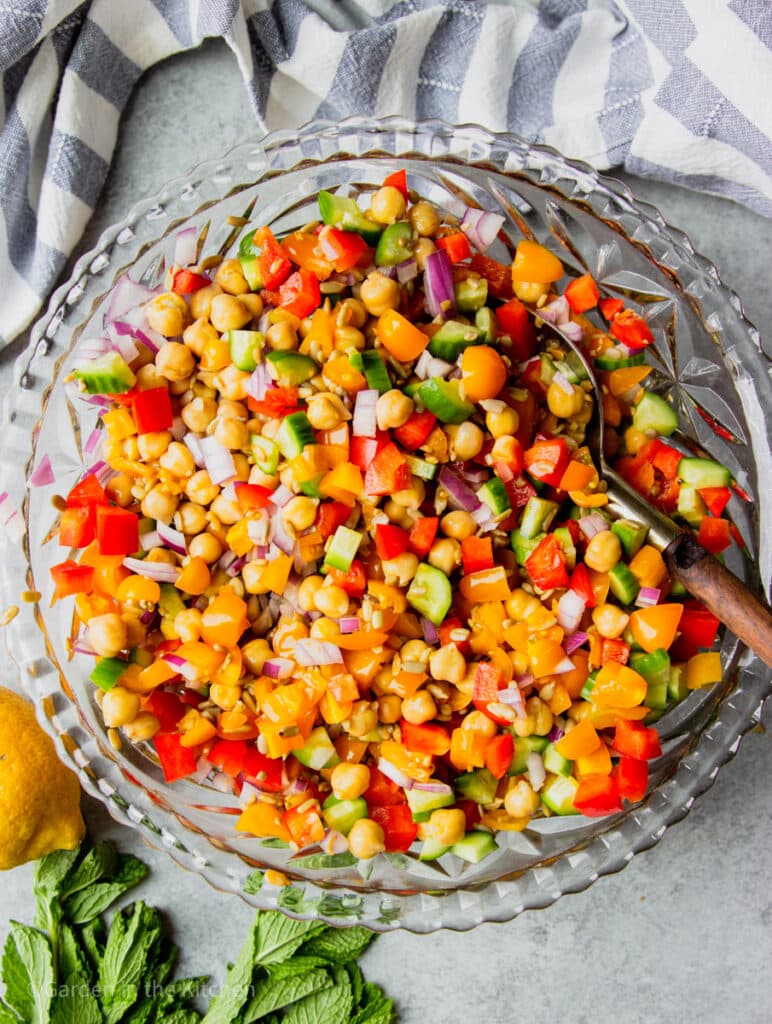 ingredients for chickpea salad tossed together in a large glass bowl.