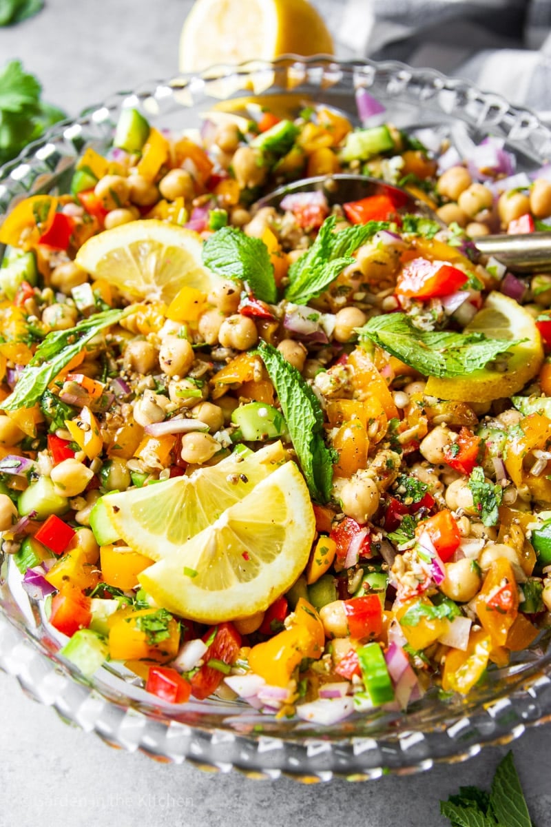close up on a lemon and mint-garnished chickpea and vegetable salad in a large glass bowl.