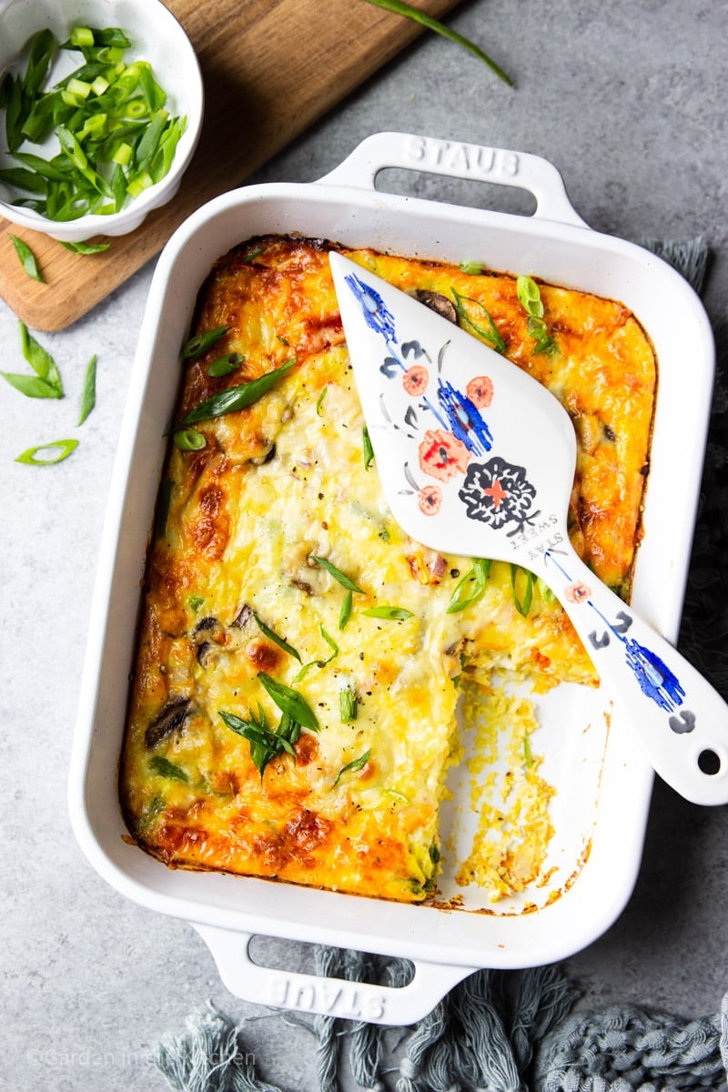 baked farmer's egg casserole in a white baking dish with a decorative pie server on top.