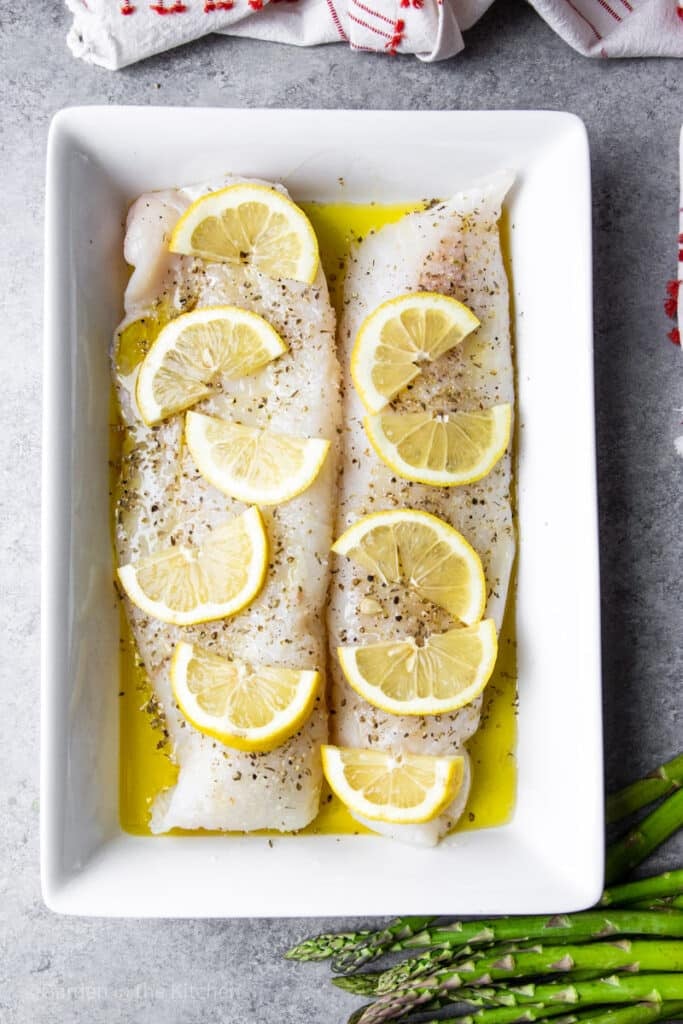 seasoned cod filets with lemon slices on a large white platter.