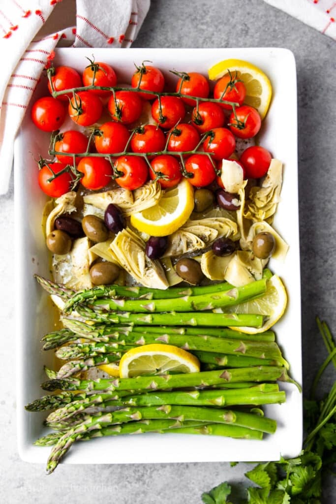 asparagus, tomatoes, artichokes, and olives on a large white platter.