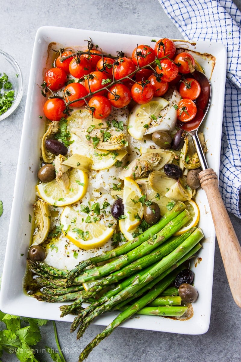 baked cod and a medley of roasted vegetables together on a large white platter.