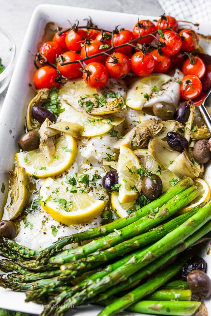 baked cod and a medley of roasted vegetables together on a large white platter.