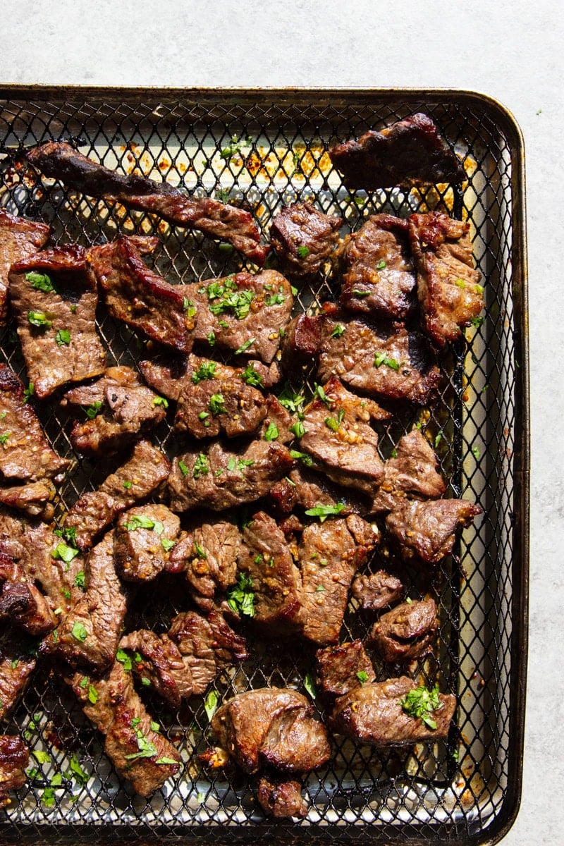 Cooked air fryer steak tips with parsley in an air fryer basket. 