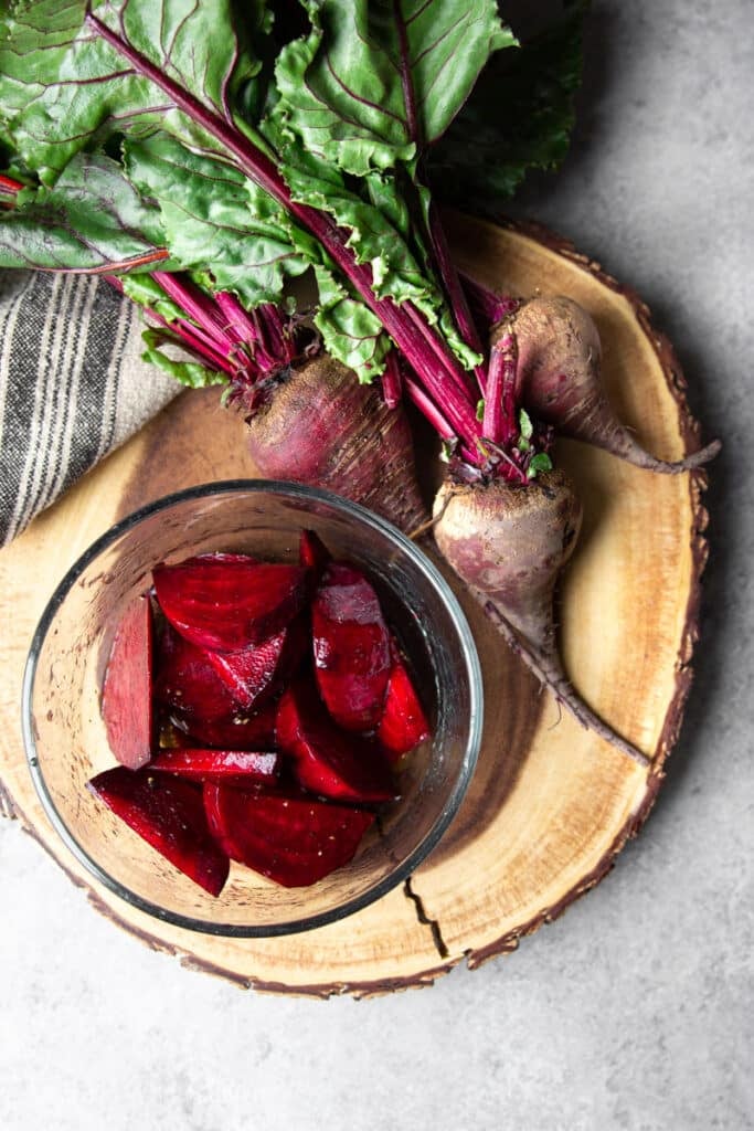 Beet root displayed on a round wooden tray. A small glass bowl with sliced and marinated beets. 