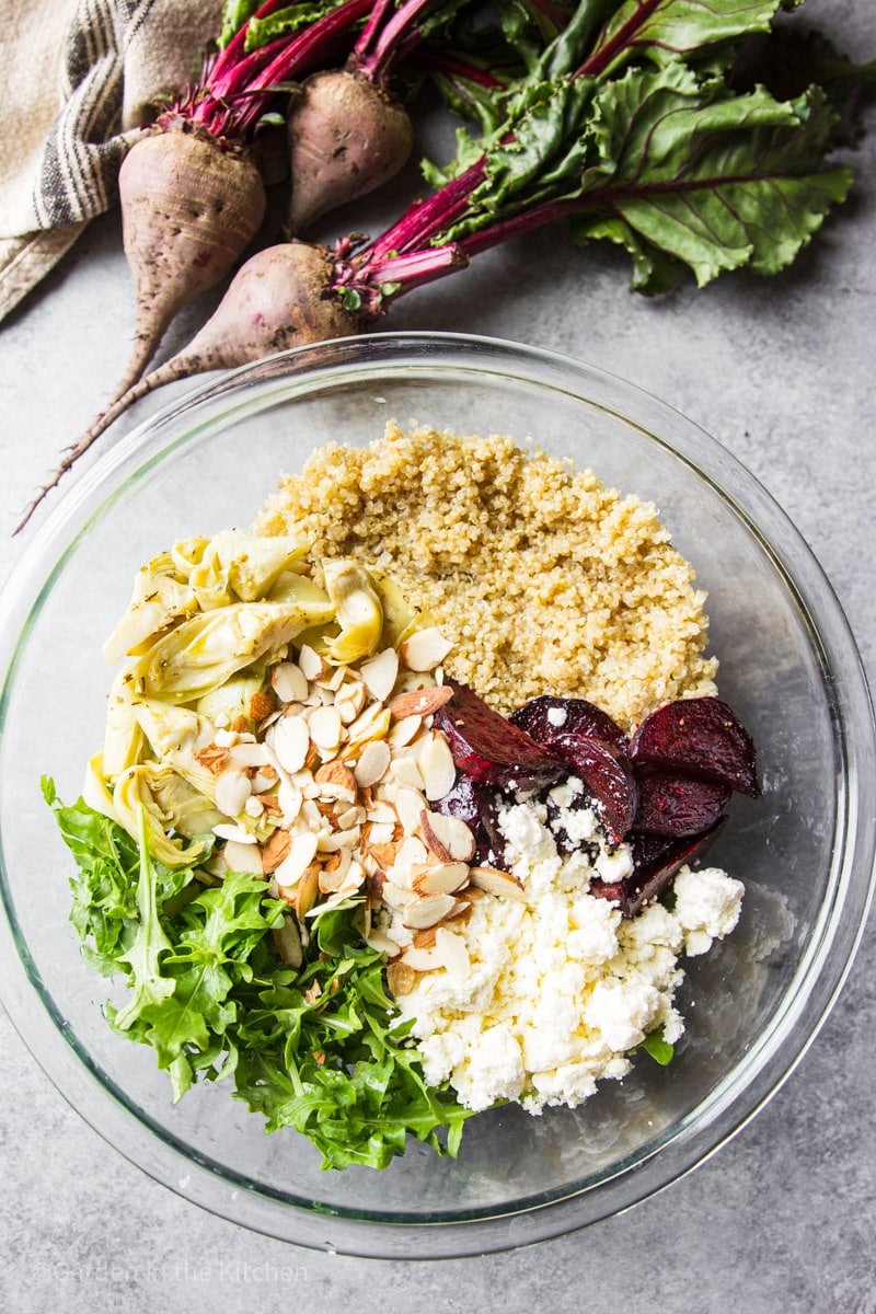 A bowl in measured ingredients for a salad. Quinoa, beet slices, feta cheese, sliced almonds and arugula. 