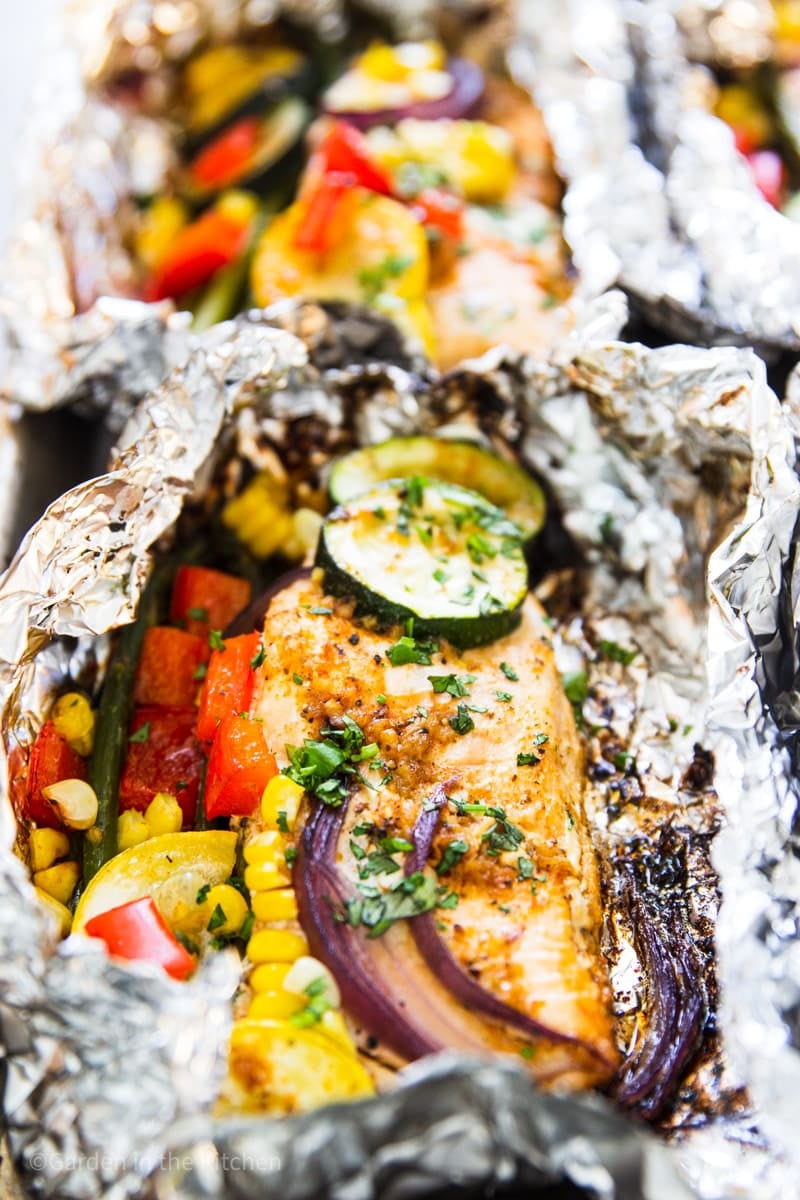 Tin foil packet with grilled salmon, red onion, red bell pepper, corn, zucchini, summer squash, asparagus and cilantro.