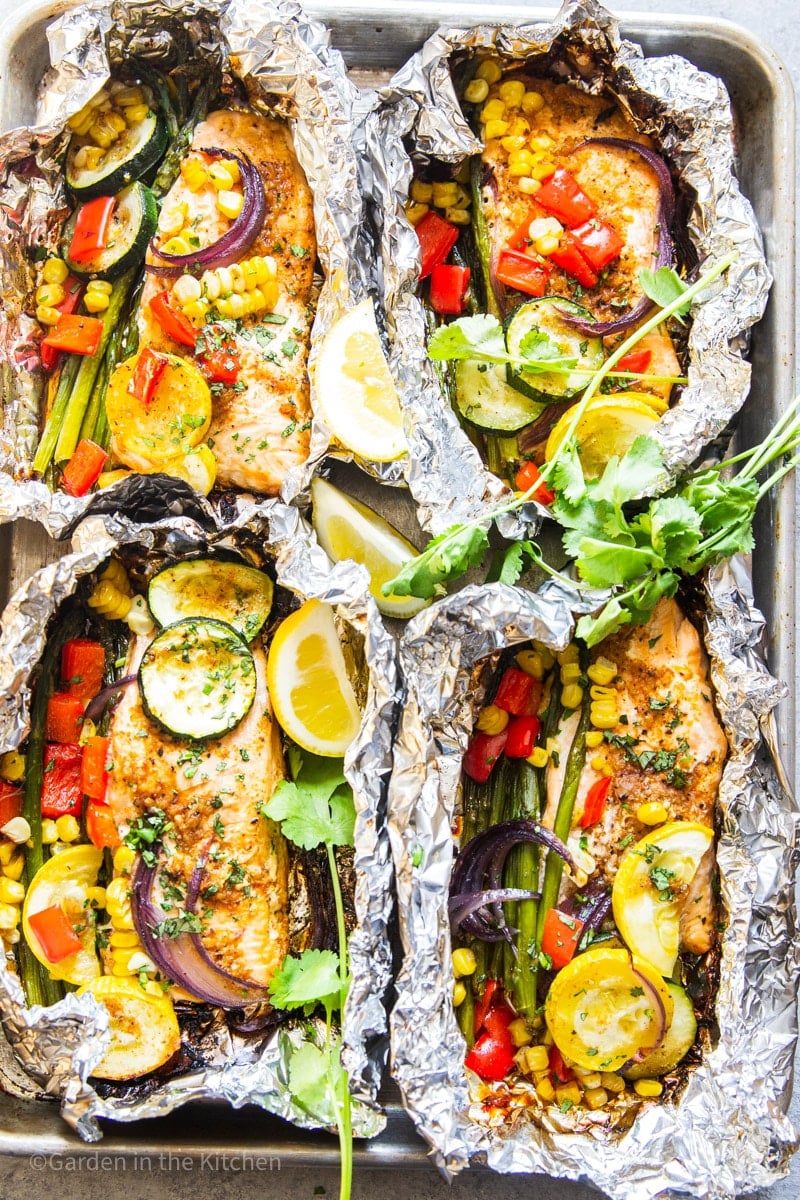 Grilled salmon and vegetables in foil. Summer squash, red onions, zucchini, red bell peppers, corn on the cob, asparagus and cilantro.