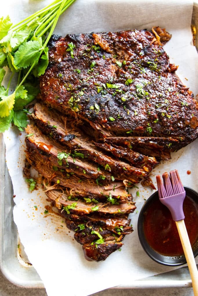 Sliced, cooked slow cooker brisket with barbeque sauce and cilantro.