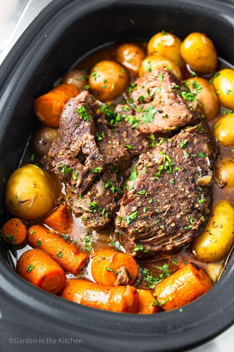 Slow cooked pot roast with baby potatoes and carrots, fresh thyme in a slow cooker.