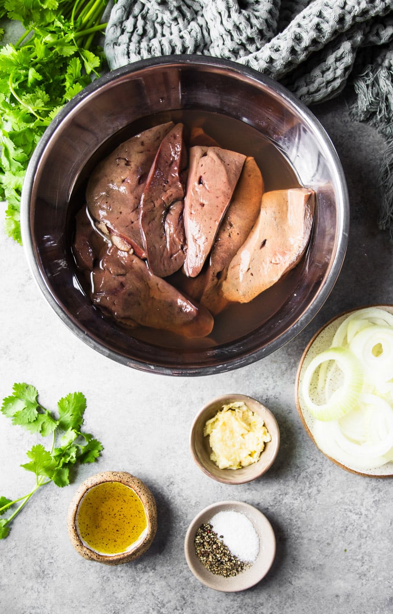 Beef liver in a stainless steel bowl marinating in vinegar, onions, garlic paste, salt and pepper, olive oil and cilantro.