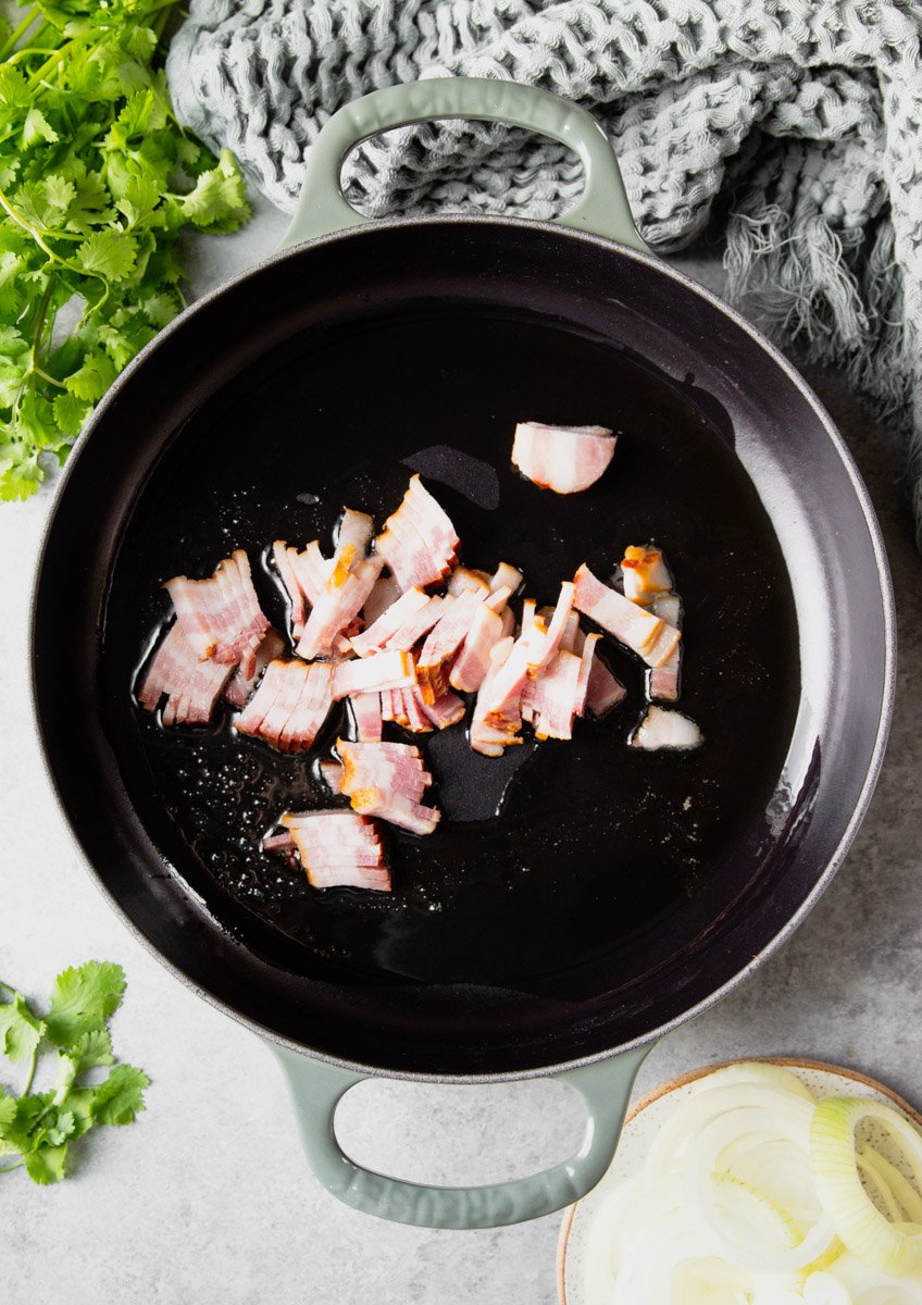 Raw bacon in a pan with oil with onions, cilantro and a grey scarf.