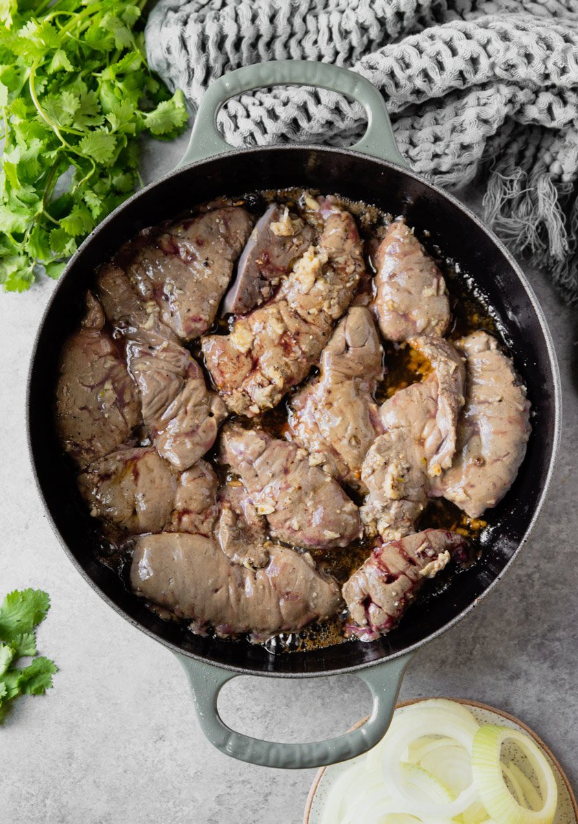 Liver in a pan with onions, cilantro and grey scarf.