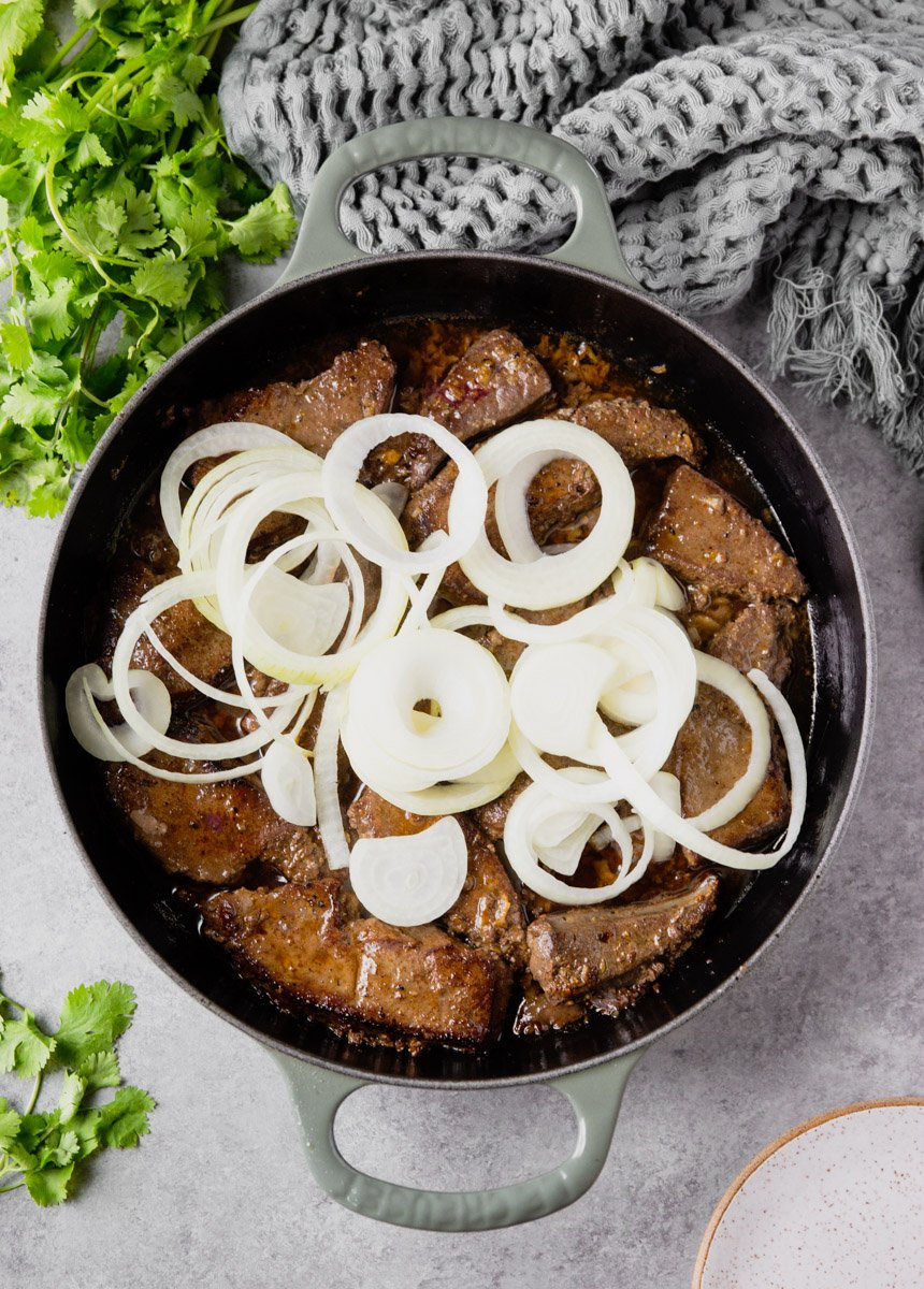 Liver in a pan with onions on top, cilantro, grey scarf.