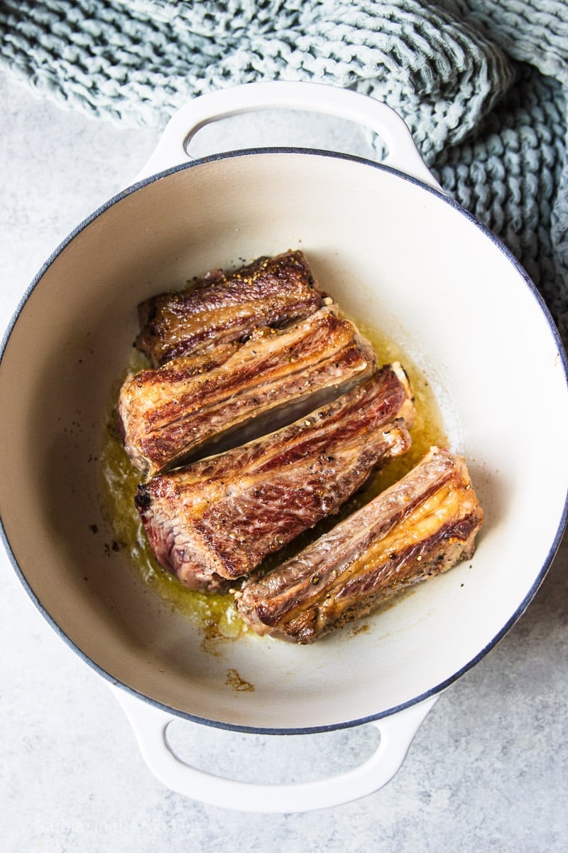 seared ribs in a white pot with a grey blanket.