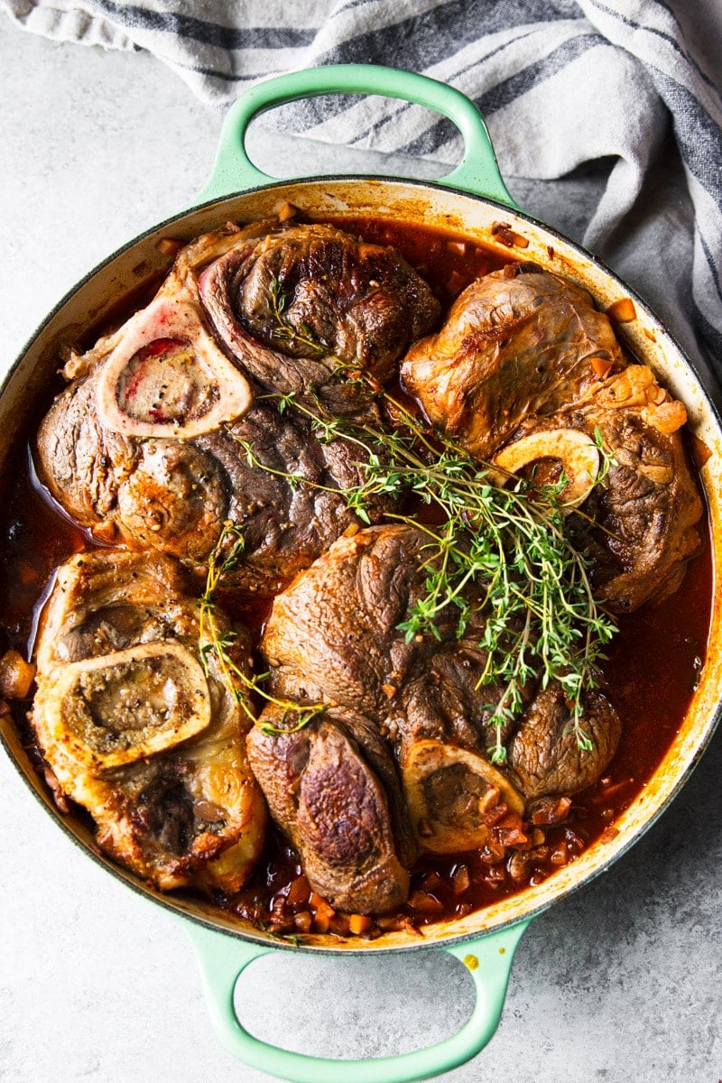 Braised beef shanks with fresh thyme in a green skillet. 