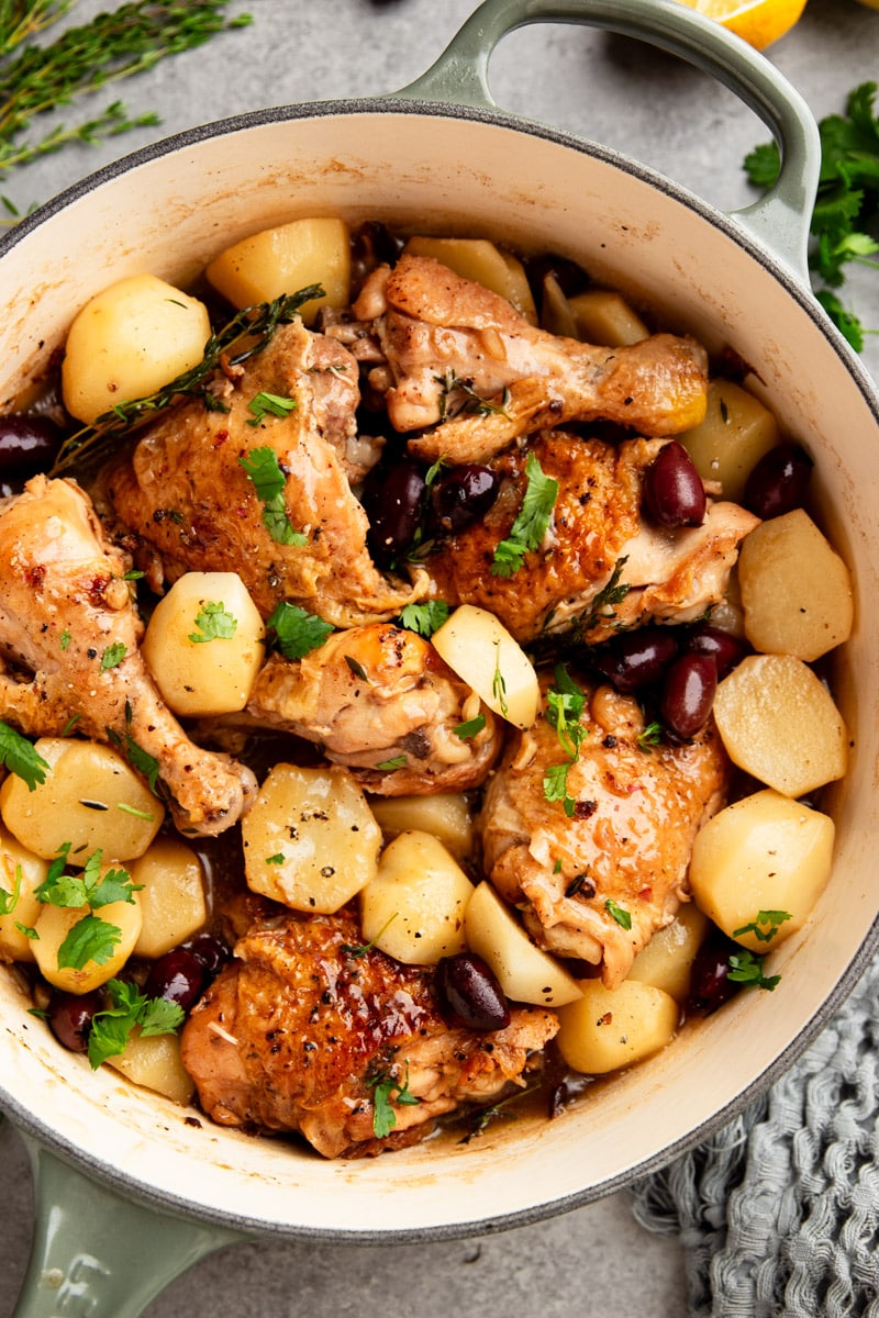 Braised chicken with potatoes, and black olives in a white pot with parsley