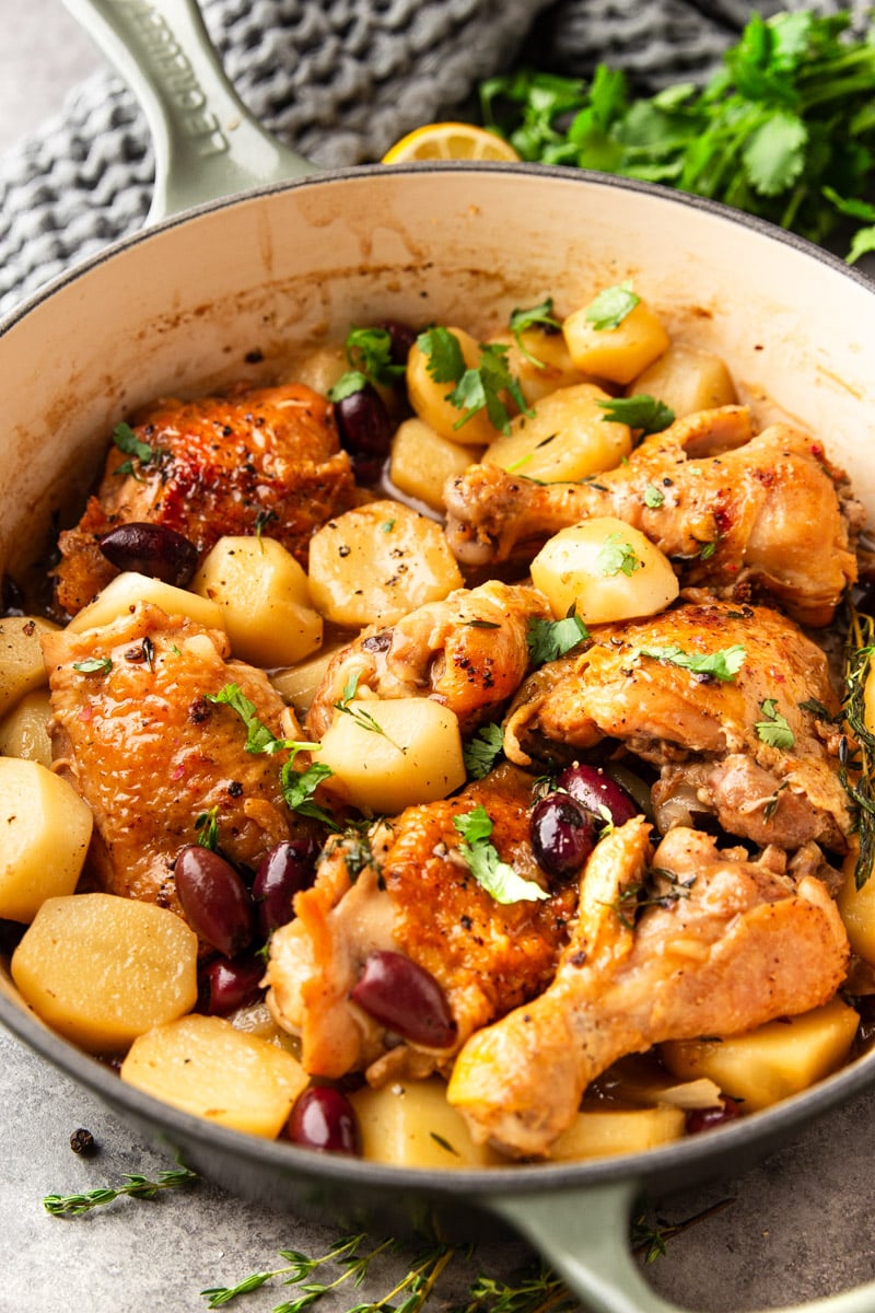 Braised chicken with potatoes, and black olives in a white pot with parsley.