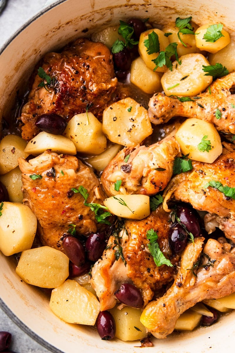 Braised chicken with potatoes, and black olives in a white pot with parsley. 