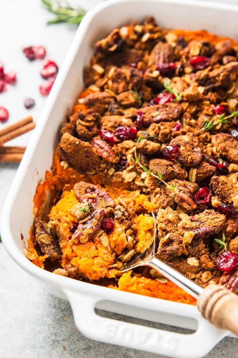 Sweet Potato Casserole in a white baking dish with cranberries, cinnamon sticks and rosemary twigs.