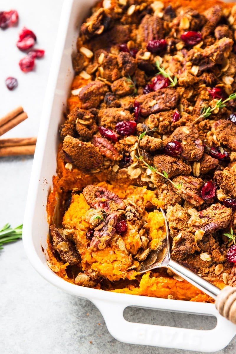 Sweet Potato Casserole in a white baking dish with cranberries, cinnamon sticks and rosemary twigs.