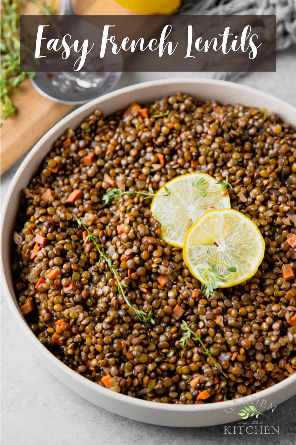 Cooked French lentils, silver spoon, lemon slices, fresh thyme, in a Le Creuset pot, wooden cutting board.
