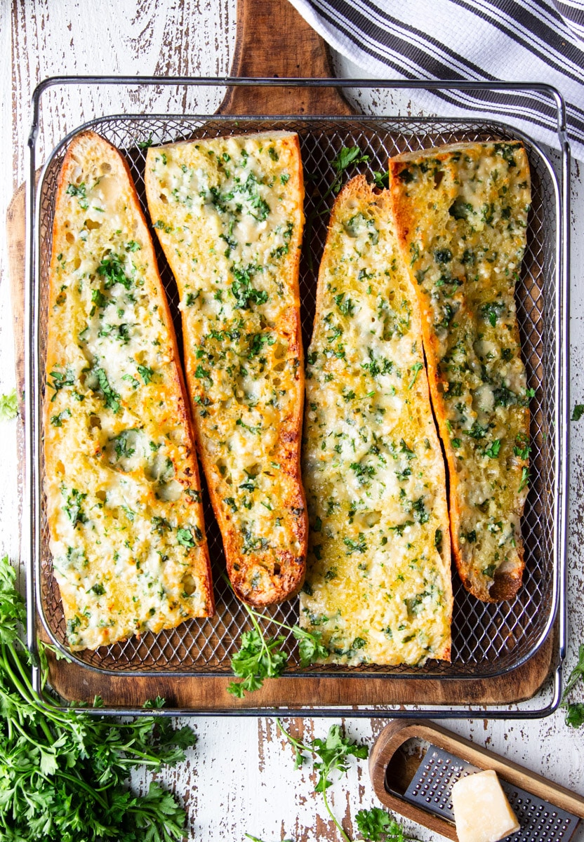 Baked air fryer garlic bread, parsley, parmesan cheese on a cheese grater, wooden cutting board.