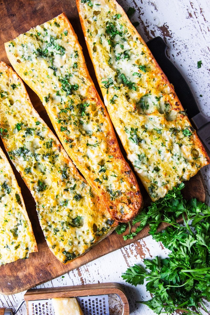 Baked air fryer garlic bread, fresh parsley on a wooden cutting board with parmesan cheese and a cheese grater. 
