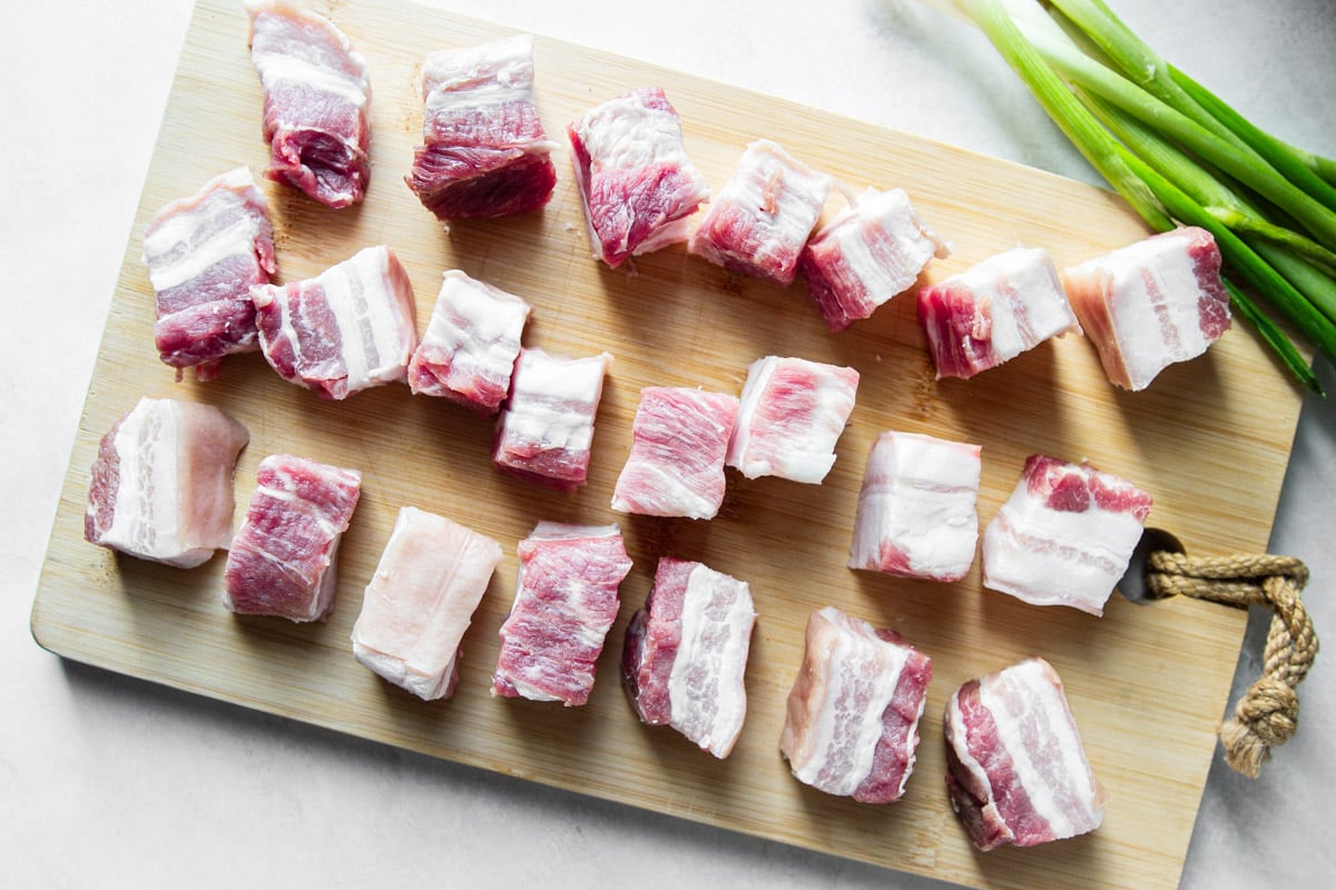 Cubed pork belly on a wooden cutting board with green onions. 