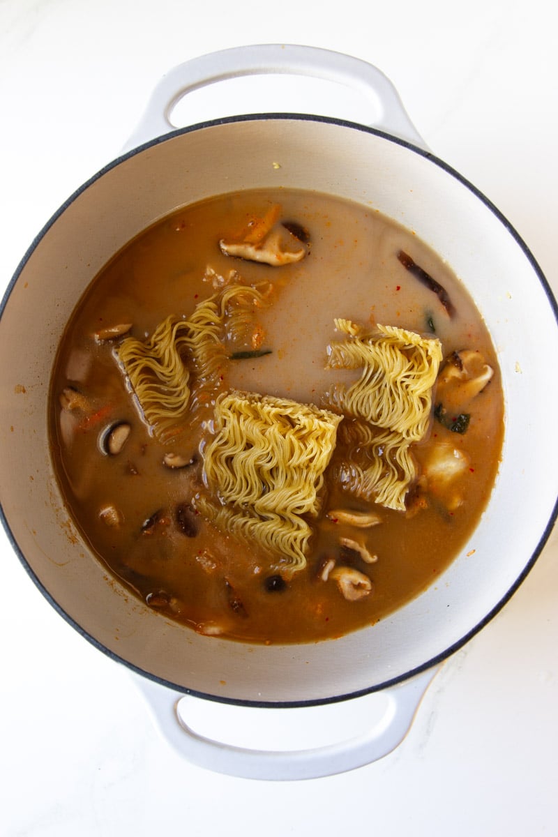 Shiitake mushrooms, ramen noodles and broth in a white pot. 