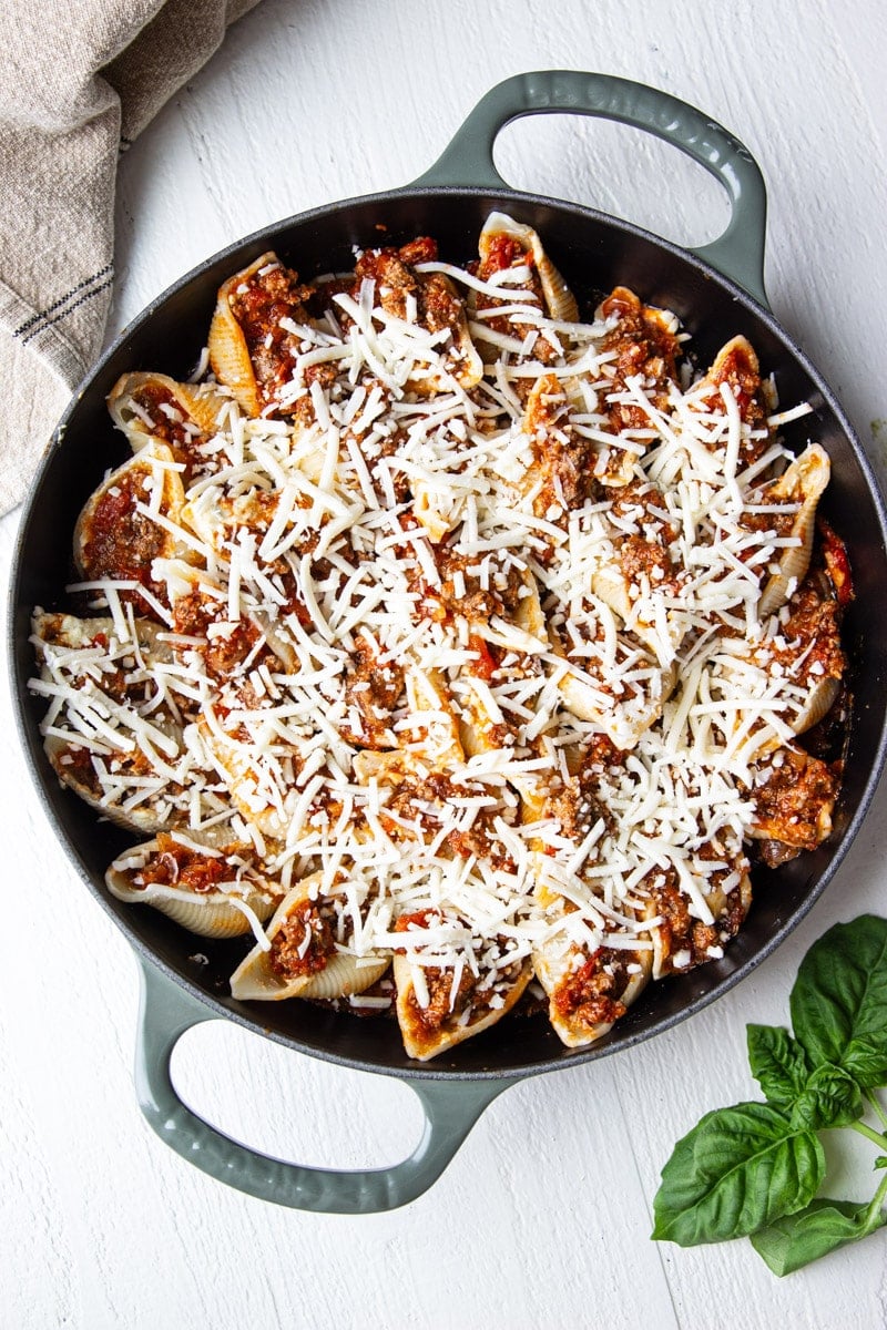 Shells stuffed with beef and topped with cheese in a cast iron skillet and fresh basil. 