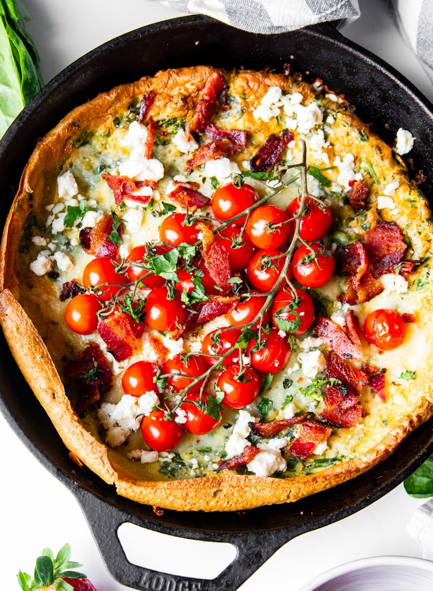 Savory Dutch baby with spinach, bacon, feta, cheddar cheese, cherry tomatoes, and bacon in a cast iron skillet. 