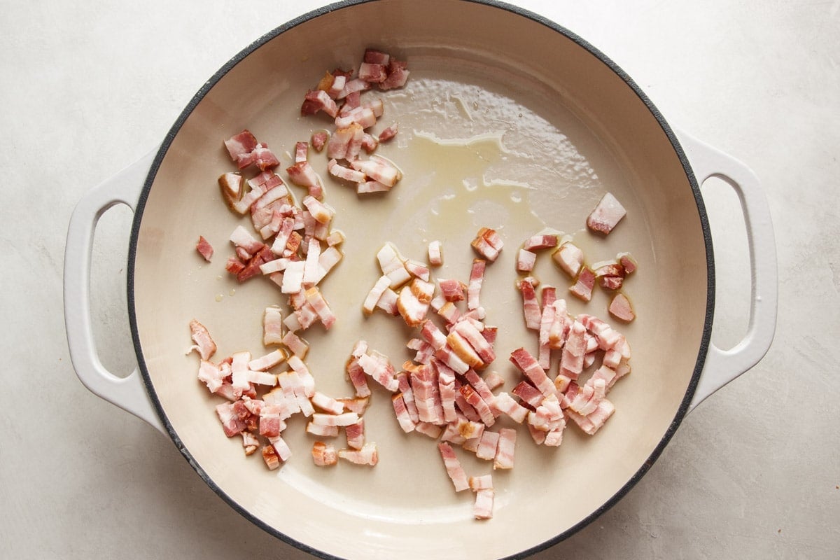 Bacon chunks in a white skillet. 