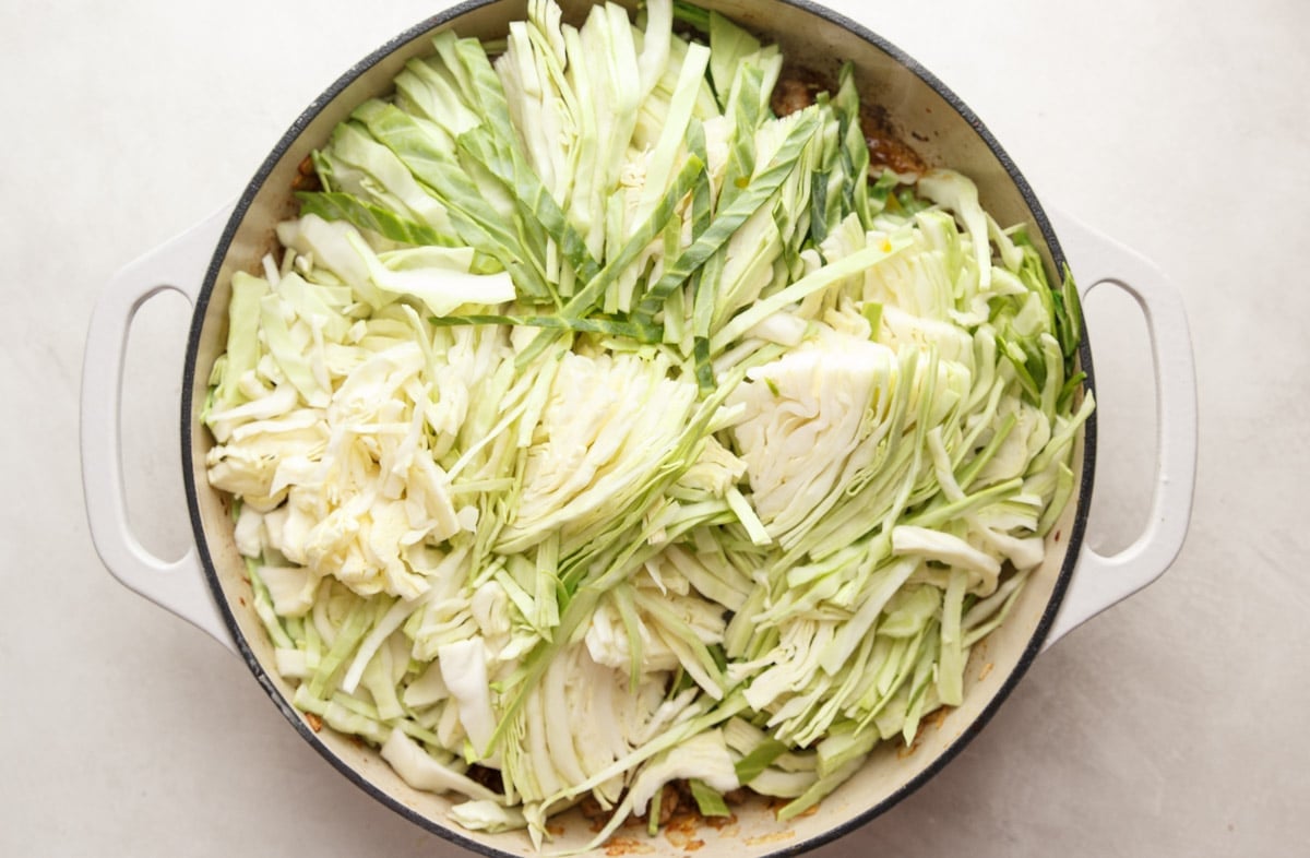 Sliced cabbage on top of the sausage mixture in the skillet. 