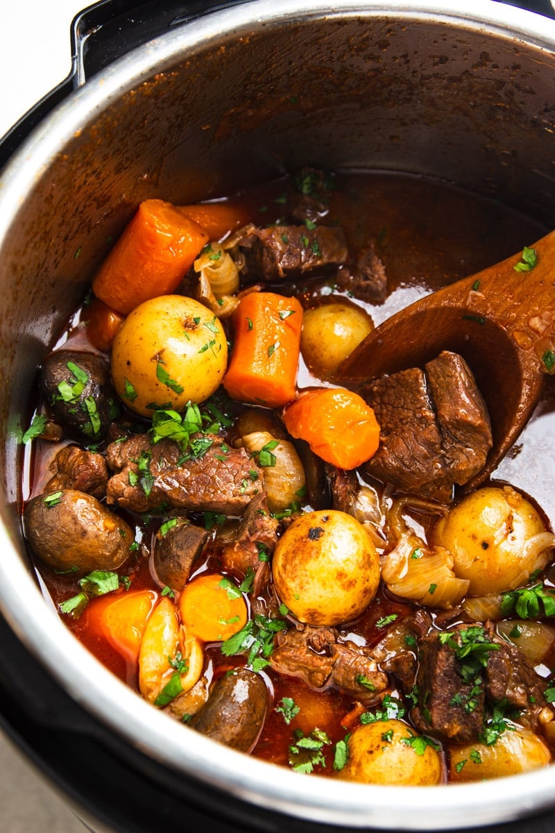 Beef bourguignon with pearl onions, carrots, baby potatoes and parsley and a wooden spoon. 