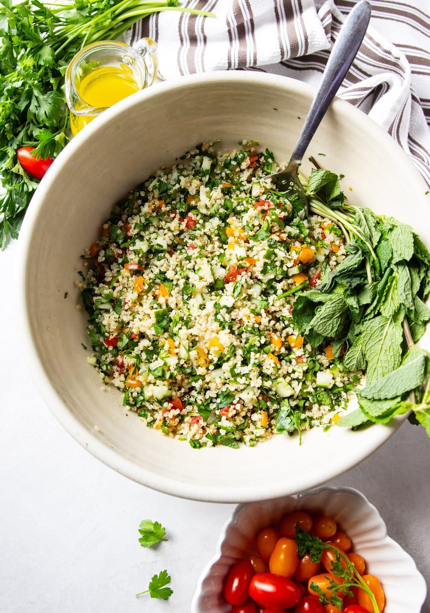 Quinoa tabbouleh, fresh mint, parsley, cherry tomatoes, olive oil and a white and brown dish towel. 