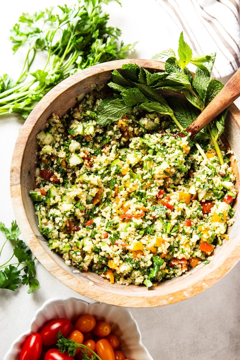 Quinoa tabbouleh and fresh mint in a wooden bowl with a wooden spoon. Fresh parsley and red cherry tomatoes. 