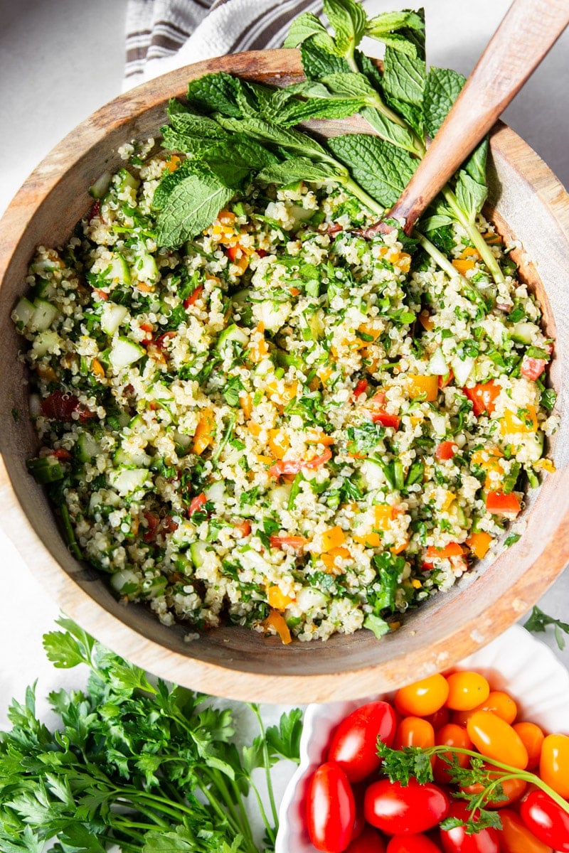 Quinoa tabbouleh with fresh mint in a wooden bowl with a wooden spoon. Red and orange cherry tomatoes and fresh parsley. 