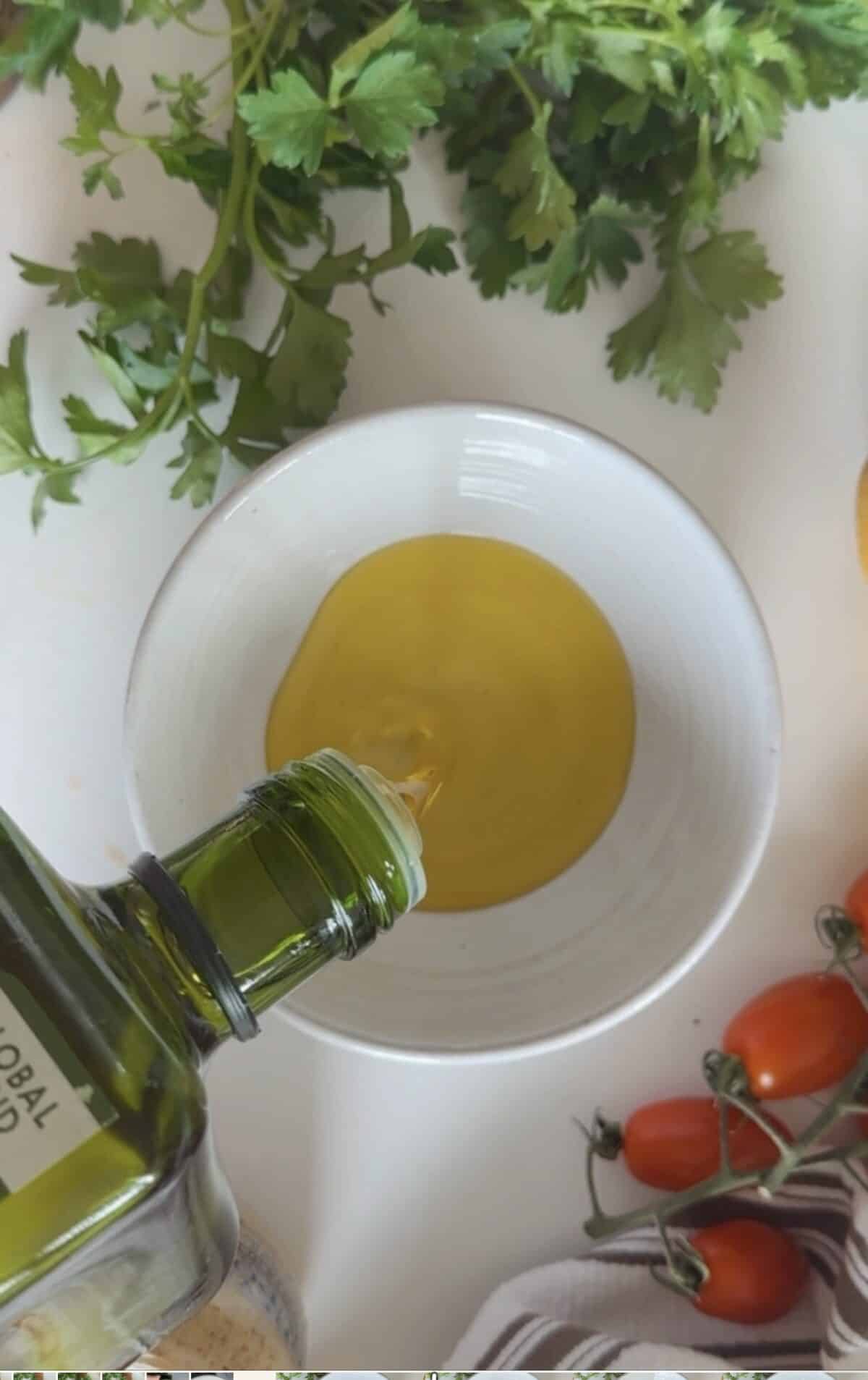 Pouring olive oil into a ramekin, cherry tomatoes and parsley. White and brown dish towel. 