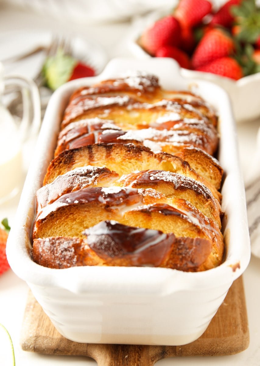 Baked Tres Leche French toast casserole in a white baking dish, strawberries. 