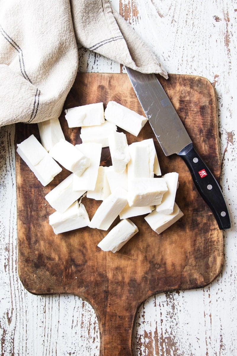 Peeled and chopped yuca on a wooden cutting board with a knife and dish towel. 