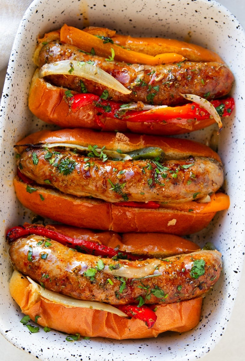 Three sausage and pepper sandwiches served in a white porcelain dish. 
