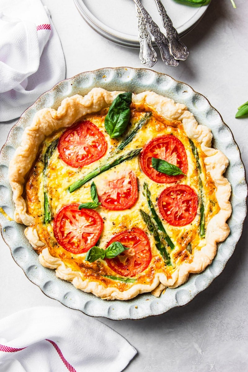 Tomato and asparagus quiche, forks, plates, fresh basil, white and red dish towel. 