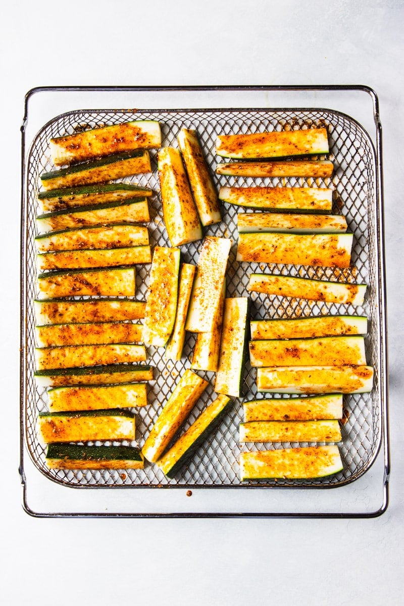 zucchini fries seasoned, in an air fryer basket