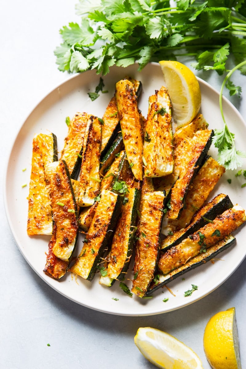 Zucchini fries, crispy and golden brown with herbs on top. Two slices of lemon.