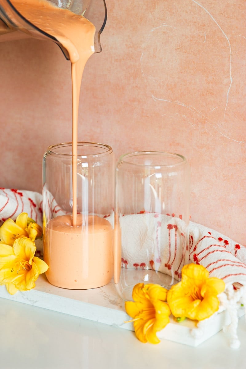 Tropical fruit smoothie, drinking glasses, white and red dish towel and yellow flowers.