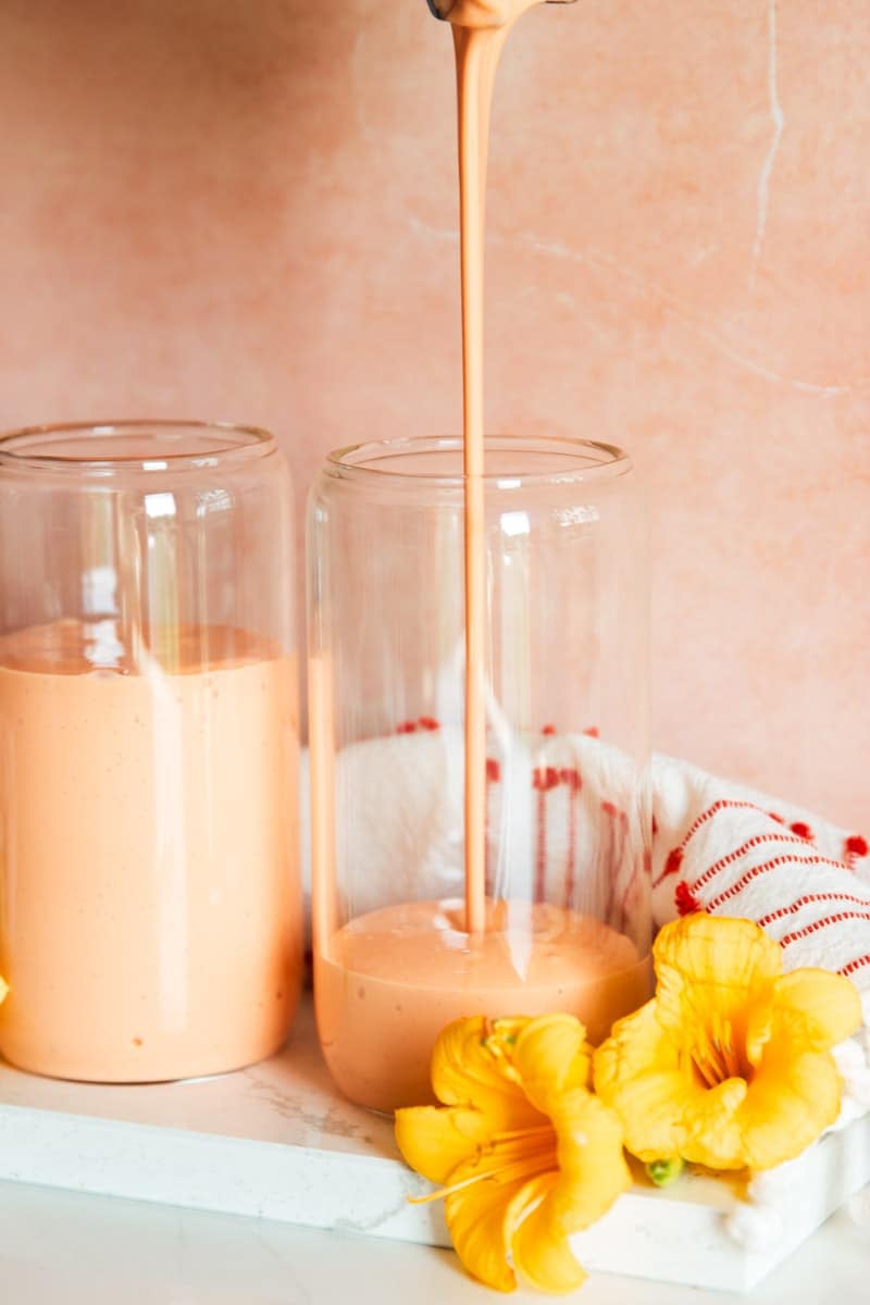 Tropical fruit smoothie, drinking glasses, white and red dish towel and yellow flowers.