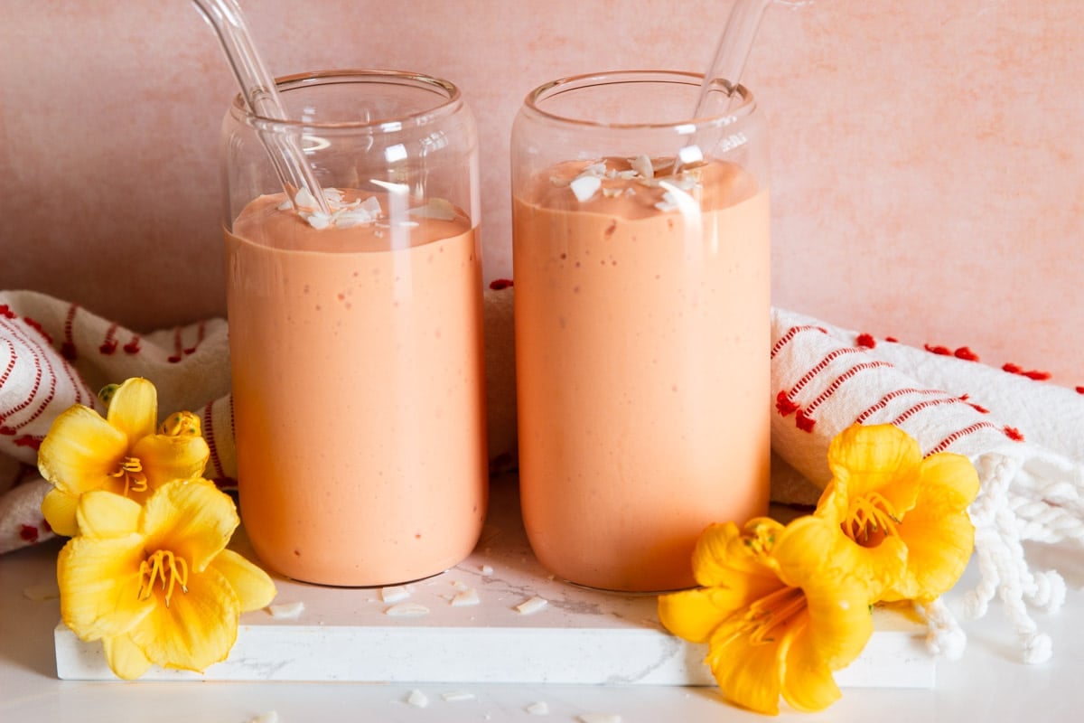 Tropical fruit smoothie, drinking glasses, white and red dish towel and yellow flowers.